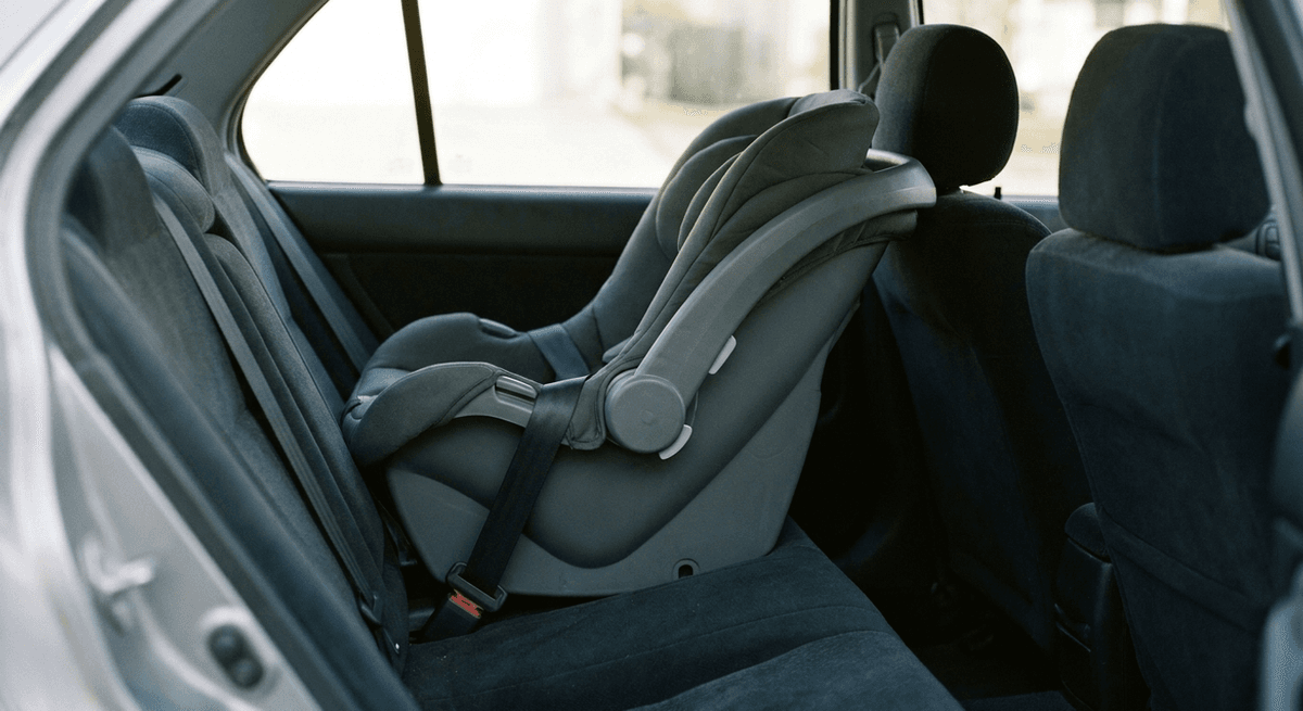 rear-facing infant car seat in grey fabric buckled into a car back seat, shown at a reclined angle