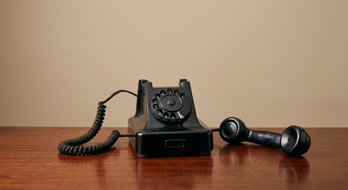 World retro rotary telephone handset lying off the hook on a mahogany surface