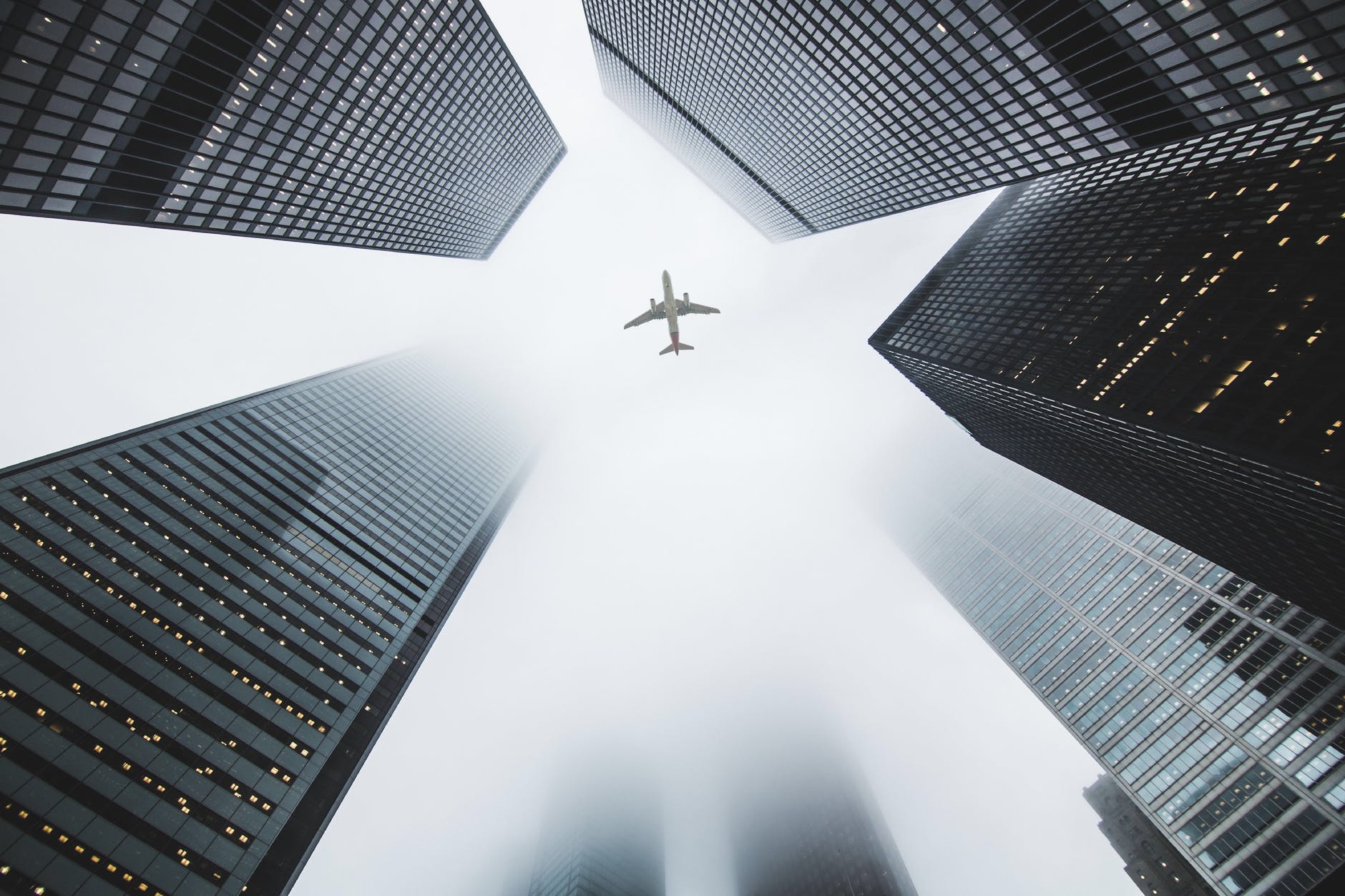 low angle photo of airplane flying over high rise buildings